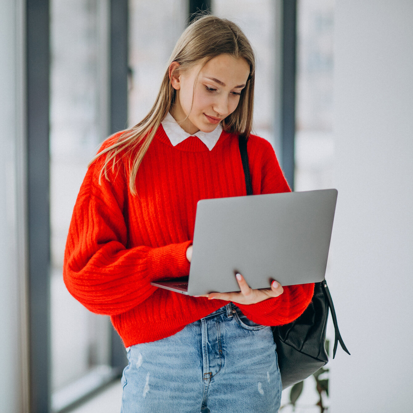 Girl student with laptop standing by the window in corridor